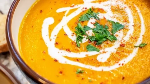 Bowl of creamy pumpkin bisque topped with herbs and served with bread
